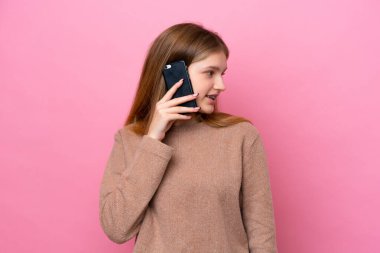 Pembe arka planda izole edilmiş genç Rus kız cep telefonuyla birileriyle sohbet ediyor.