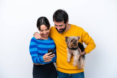 Beyaz arka planda köpeği tutan genç İspanyol kadın cep telefonuyla mesaj ya da e-posta yolluyor.
