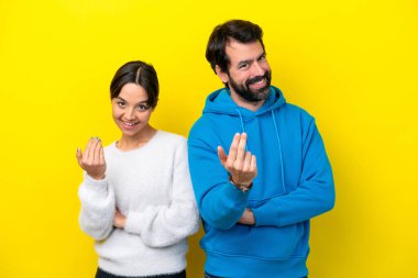 Young caucasian couple isolated on yellow background inviting to come with hand