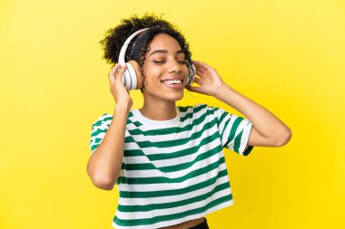 Genç Afrikalı Amerikalı kadın sarı arka planda izole edilmiş müzik dinliyor ve şarkı söylüyor.