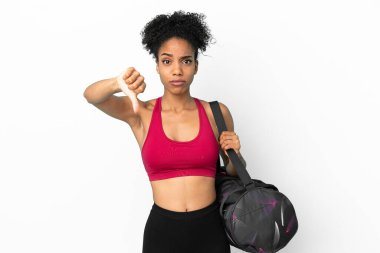 Spor çantalı genç Afro-Amerikan kadın mavi arka planda izole edilmiş, olumsuz ifadeli baş parmağını gösteriyor.