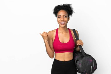 Spor çantalı genç Afro-Amerikan kadın mavi arka planda izole edilmiş bir şekilde bir ürünü sunmak için kenarı işaret ediyor.