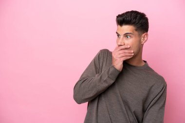 Pembe arka planda izole edilmiş genç beyaz adam yan tarafa bakarken sürpriz jest yapıyor.