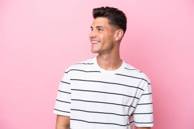 Pembe arka planda izole edilmiş genç beyaz adam yana bakıyor ve gülümsüyor.