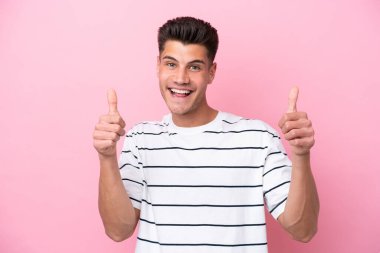 Pembe arka planda izole edilmiş genç beyaz bir adam baş parmak hareketi yapıyor.