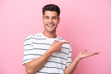 Pembe arka planda izole edilmiş genç beyaz bir adam bir ilan vermek için avucunun içinde hayali bir fotokopi makinesi tutuyor.