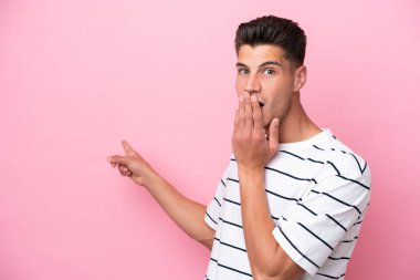 Pembe arka planda izole edilmiş genç beyaz bir adam, sürpriz bir ifadeyle işaret ederken...
