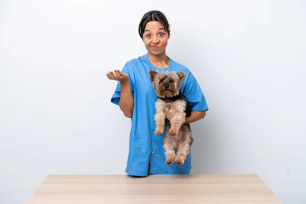 Young veterinarian woman with dog on a table isolated on white background making doubts gesture while lifting the shoulders