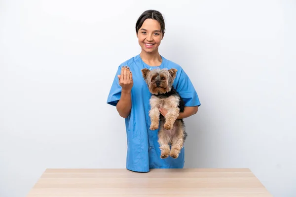 Young veterinarian woman with dog on a table isolated on white background inviting to come with hand. Happy that you came