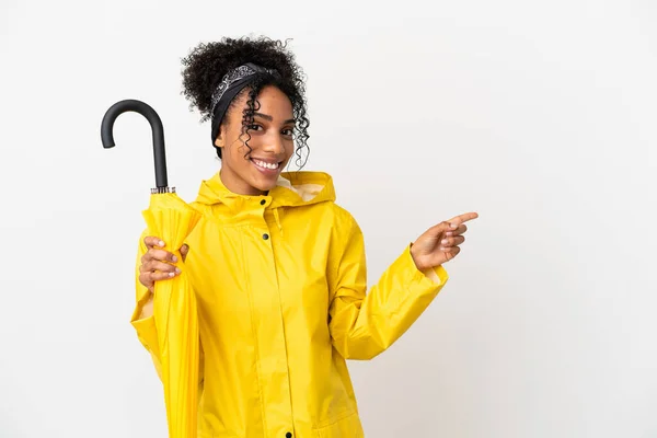 サイドに指を指す白い背景にレインプルーフコートと傘を持つ若い女性 — ストック写真