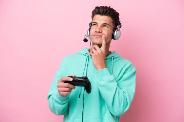 Pembe arka planda izole edilmiş bir bilgisayar oyunu kontrolörüyle oynayan yakışıklı beyaz bir adam.