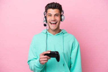 Pembe arka planda izole edilmiş bir bilgisayar oyunu kontrolörüyle oynayan yakışıklı beyaz bir adam. Sürpriz bir yüz ifadesi var.