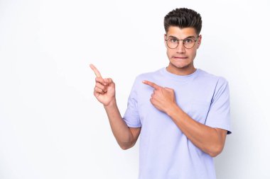 Beyaz arka planda izole edilmiş genç beyaz adam korkmuş ve kenarı işaret ediyor.