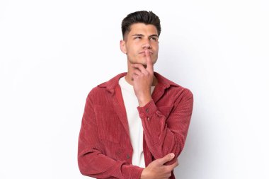 Beyaz arka planda izole edilmiş genç beyaz adam yukarı bakarken şüpheleri var.