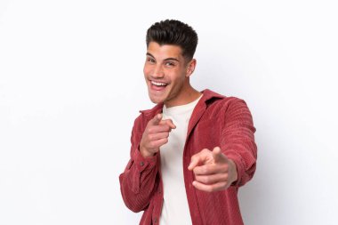 Beyaz arka planda izole edilmiş genç beyaz adam ön tarafı işaret ediyor ve gülümsüyor.