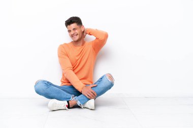 Yerde oturan genç adam beyaz arka planda boynu ağrıyan izole bir şekilde oturuyor.