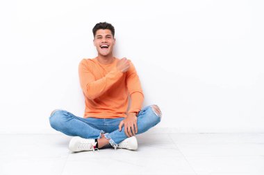 Yerde oturan genç adam beyaz arka planda tek başına zaferi kutluyor.