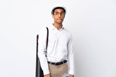 African American architect man with helmet and holding blueprints over isolated white background _ having doubts while looking up