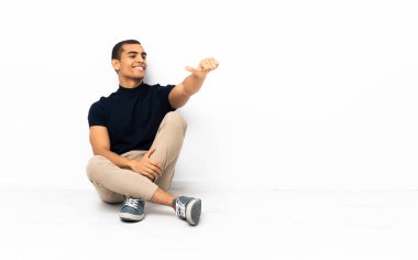 Afro-Amerikalı bir adam yerde oturuyor ve baş parmak işareti yapıyor.