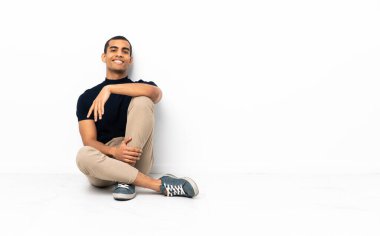 Afrika kökenli Amerikalı adam yerde oturuyor ve kollarını ön cephede kavuşturuyor.