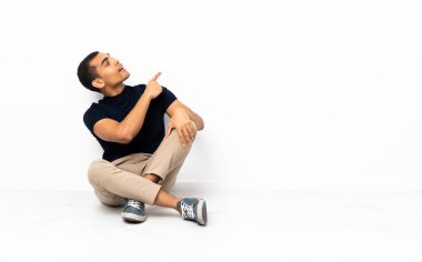 Afro-Amerikalı bir adam yerde oturmuş işaret parmağıyla işaret ediyor.