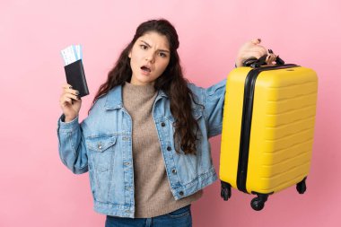 Young woman over isolated pink background in vacation with travel suitcase