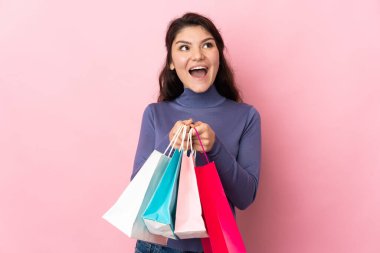 Pembe arka planda izole edilmiş genç Rus kız elinde alışveriş torbalarıyla şaşırmış.