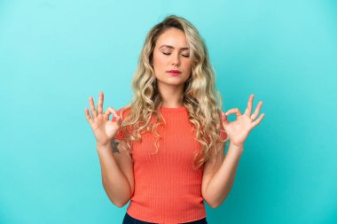 Genç Brezilyalı kadın Zen pozunda mavi arka planda izole edilmiş.