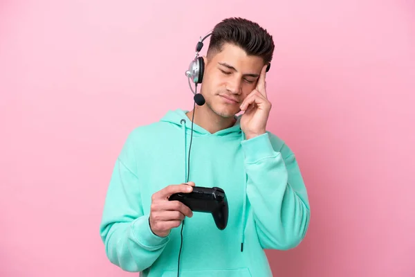 年轻英俊的高加索男子与一个带粉色背景的头痛患者隔离的电子游戏控制器玩耍 — 图库照片