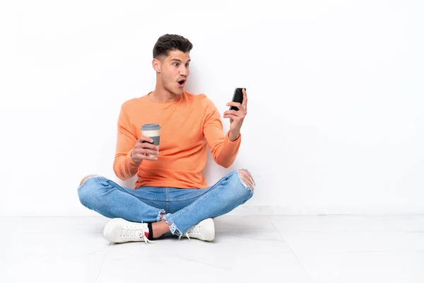 Joven Sentado Suelo Aislado Sobre Fondo Blanco Sosteniendo Café Para —  Fotos de Stock