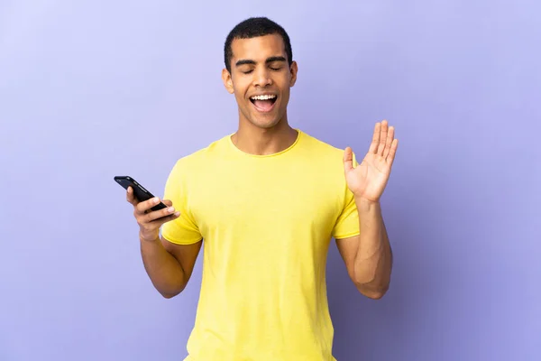 African American Man Isolated Purple Background Using Mobile Phone Laughing — Stock Photo, Image