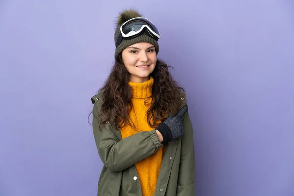 俄罗斯少女 戴着雪板眼镜 与紫色背景隔离 指向侧面来展示一种产品 — 图库照片