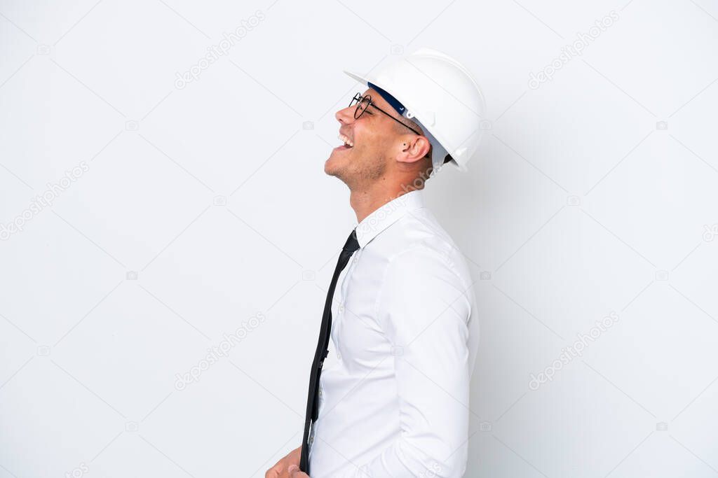 Young architect caucasian man with helmet and holding blueprints isolated on white background laughing in lateral position