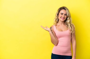 Sarı arka planda izole edilmiş genç Brezilyalı bir kadın gülümseyerek bir fikir sunuyor.