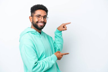 Beyaz arka planda izole edilmiş genç Brezilyalı bir adam parmak göstererek bir ürün sunuyor.