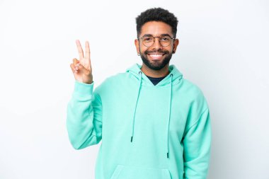 Beyaz arka planda izole edilmiş genç Brezilyalı adam gülümsüyor ve zafer işareti gösteriyor