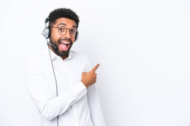 Tele pazarlamacı Brezilyalı adam beyaz arka planda izole edilmiş kulaklıkla çalışıyor. Şaşırmış ve işaret ediyor.