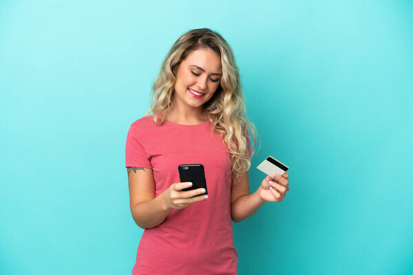 Young Brazilian woman isolated on blue background buying with the mobile with a credit card