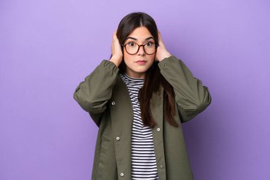 Mor arka planda izole edilmiş genç Brezilyalı kadın hayal kırıklığına uğramış ve kulaklarını kapatmış.