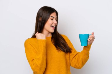 Genç Brezilyalı kadın elinde bir fincan kahveyle beyaz arka planda izole bir şekilde zaferi kutluyor.