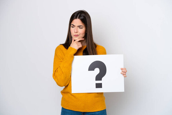 Young Brazilian woman isolated on white background holding a placard with question mark symbol and thinking