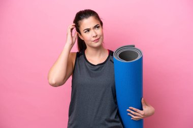 Genç Brezilyalı spor kadın yoga derslerine giderken elinde pembe arka planda izole edilmiş bir minder tutarken şüpheleri vardı.