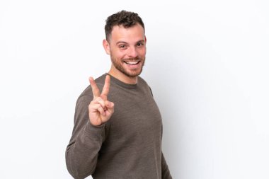 Beyaz arka planda izole edilmiş genç Brezilyalı adam gülümsüyor ve zafer işareti gösteriyor