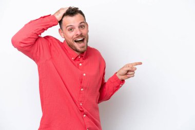 Beyaz arka planda izole edilmiş genç Brezilyalı şaşırmış ve parmağıyla kenarı işaret ediyor.