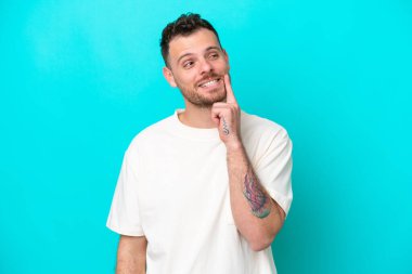 Genç Brezilyalı bir adam mavi arka planda izole edilmiş bir şekilde yukarı bakarken bir fikir düşünüyor.