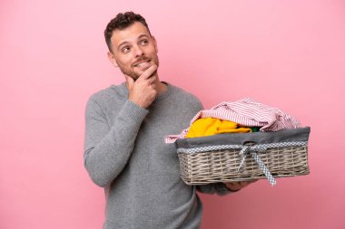 Genç Brezilyalı bir adam pembe arka planda izole edilmiş bir sepet tutuyor gülümserken yukarı bakıyor.