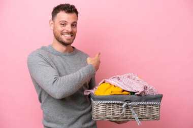 Genç Brezilyalı bir adam pembe arka planda izole edilmiş bir çamaşır sepeti tutuyor.