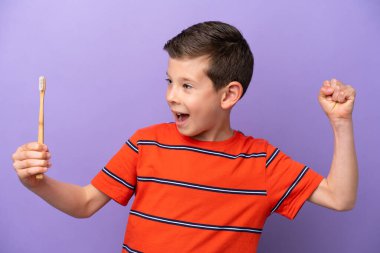 Mor arka planda dişlerini fırçalayan küçük çocuk zaferi kutluyor.