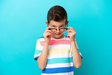 Mavi arka planda izole edilmiş küçük bir çocuk. Neşeli gözlüklü.