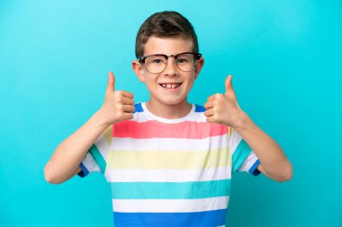 Küçük çocuk mavi arka planda gözlüklü ve baş parmağıyla izole edilmiş.